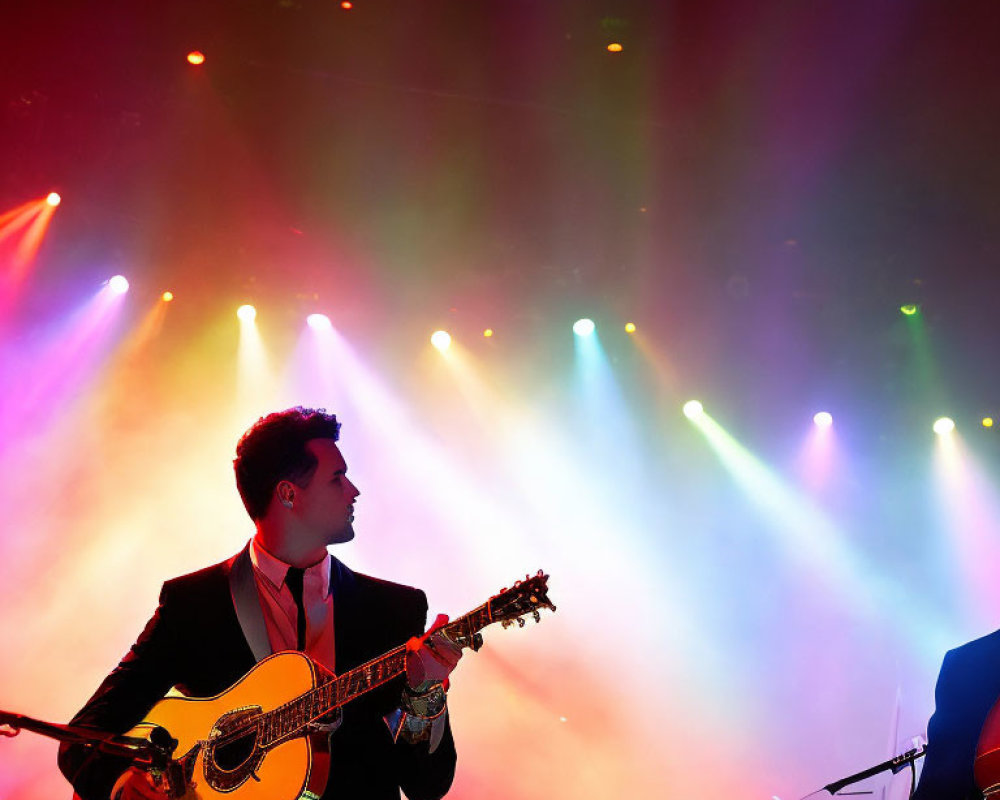 Musician plays acoustic guitar on stage under vibrant stage lights