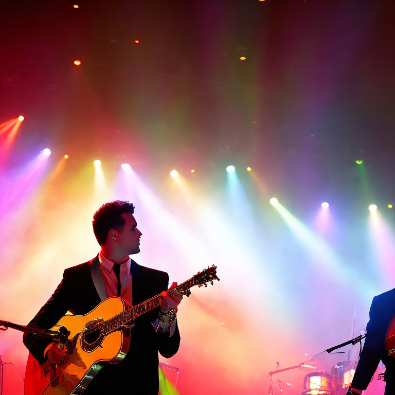 Musician plays acoustic guitar on stage under vibrant stage lights