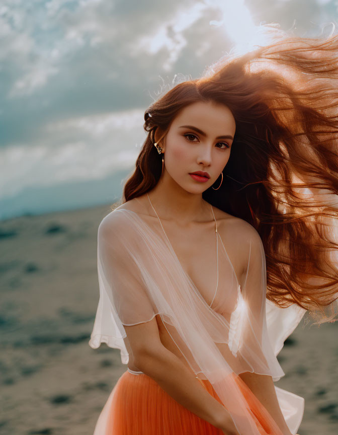 Woman with flowing hair in pale top and orange skirt in windy landscape.