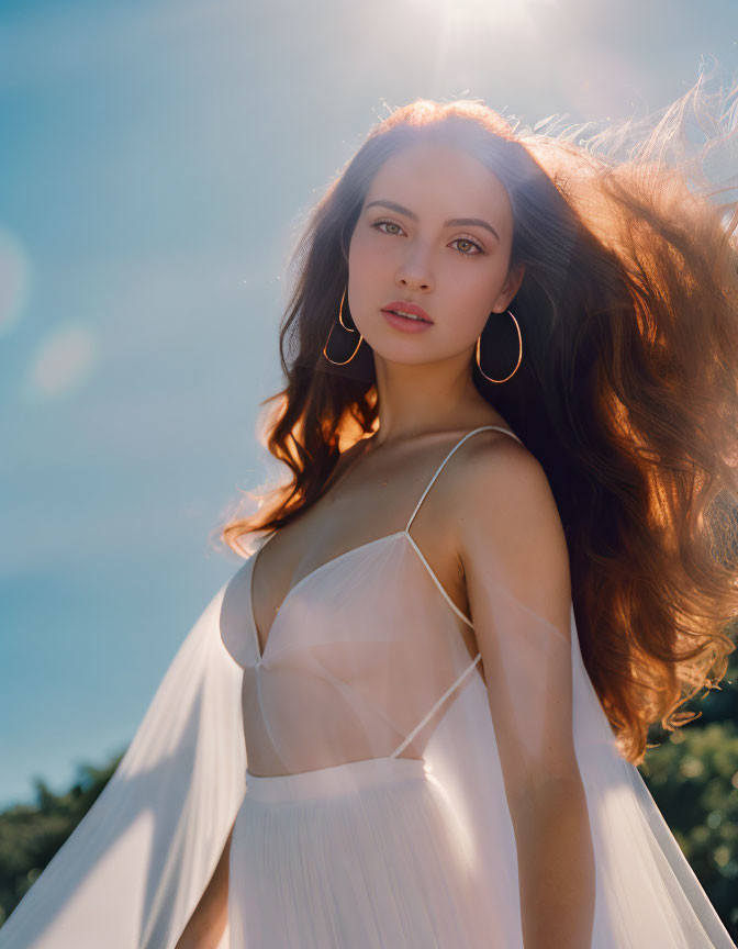 Woman in white dress with flowing hair and hoop earrings under sunlight glare.