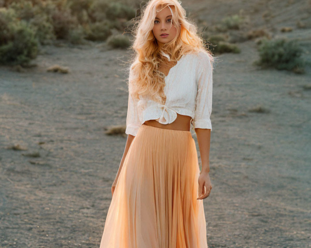 Blonde woman in white crop top and peach skirt in desert landscape