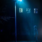 People silhouettes in foggy, dimly lit night street with blue and red lights