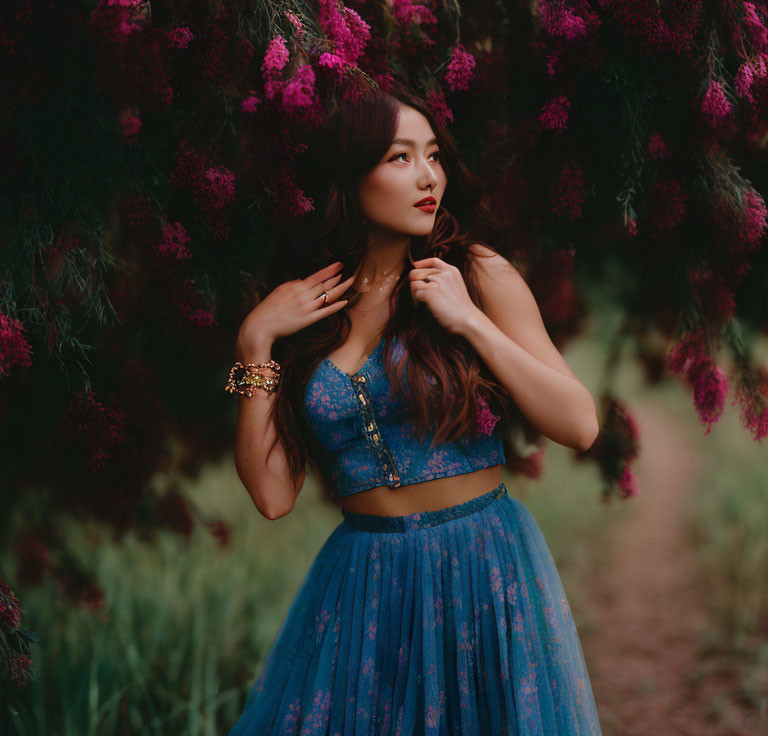 Woman in Blue Dress Standing Under Pink Flowers with Thoughtful Expression