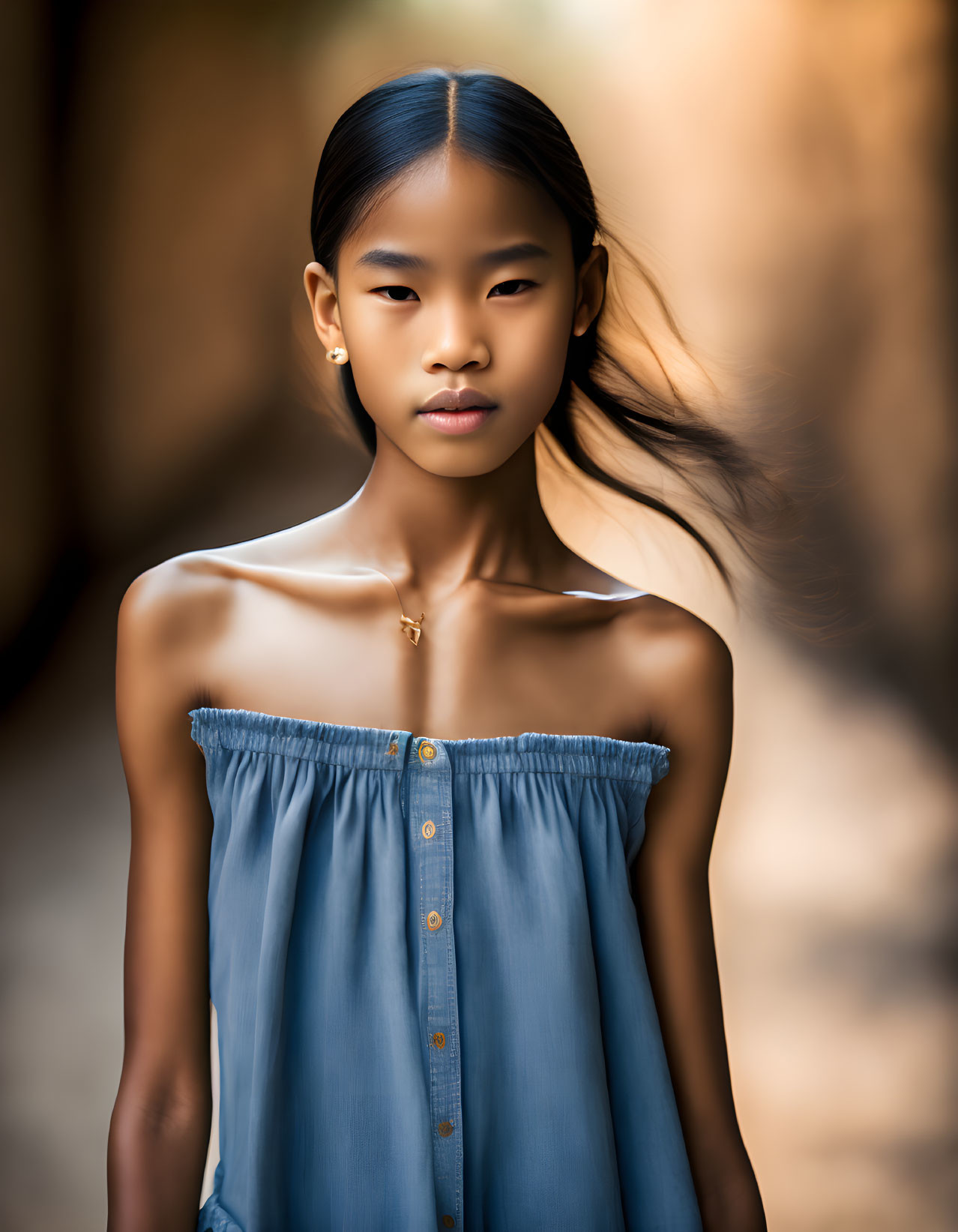 Young girl in blue dress with cross necklace in blurred background