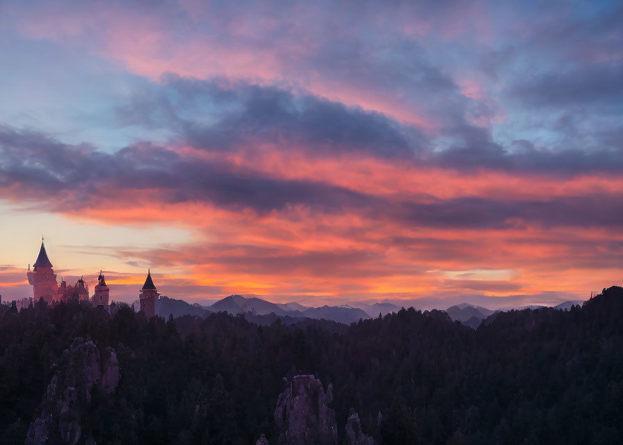 Castle silhouette against vibrant sunset with pink and orange clouds over forested mountains.