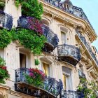 European-style building with ornate balconies and lush greenery & purple flowers against blue sky