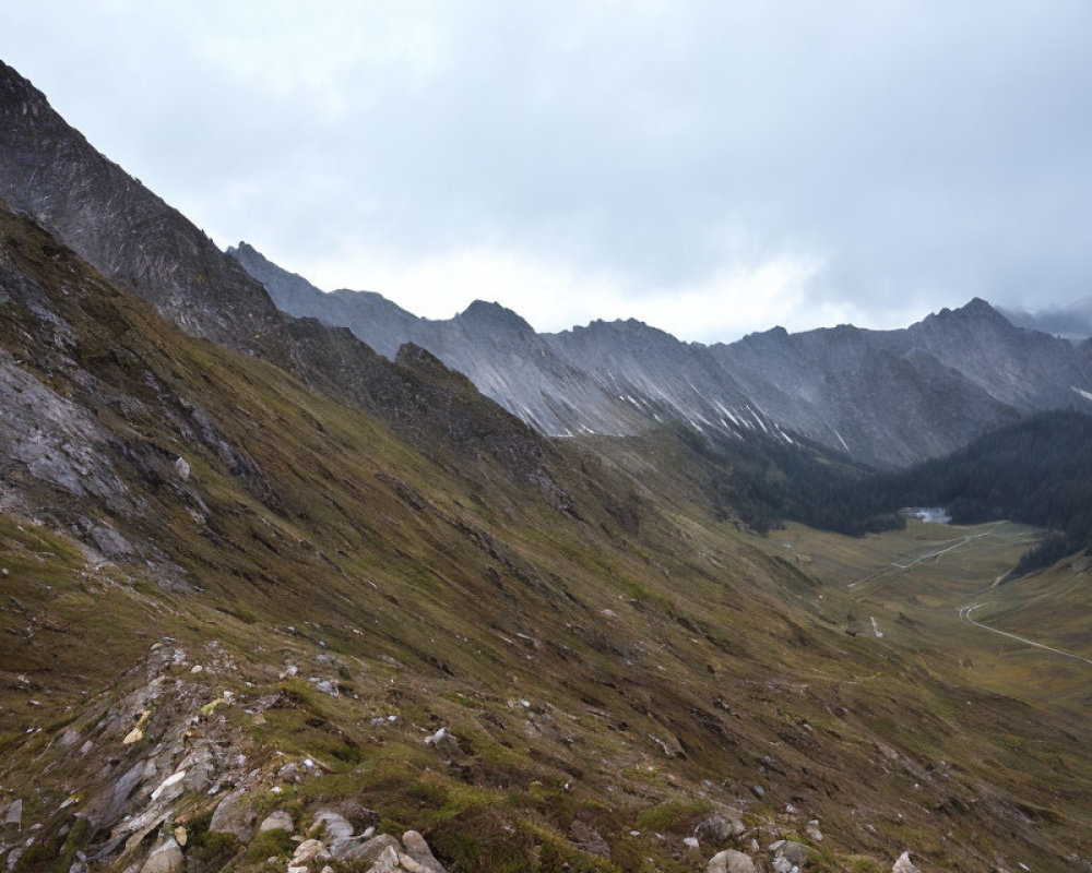 Overcast rugged mountain landscape with steep slopes and winding road.