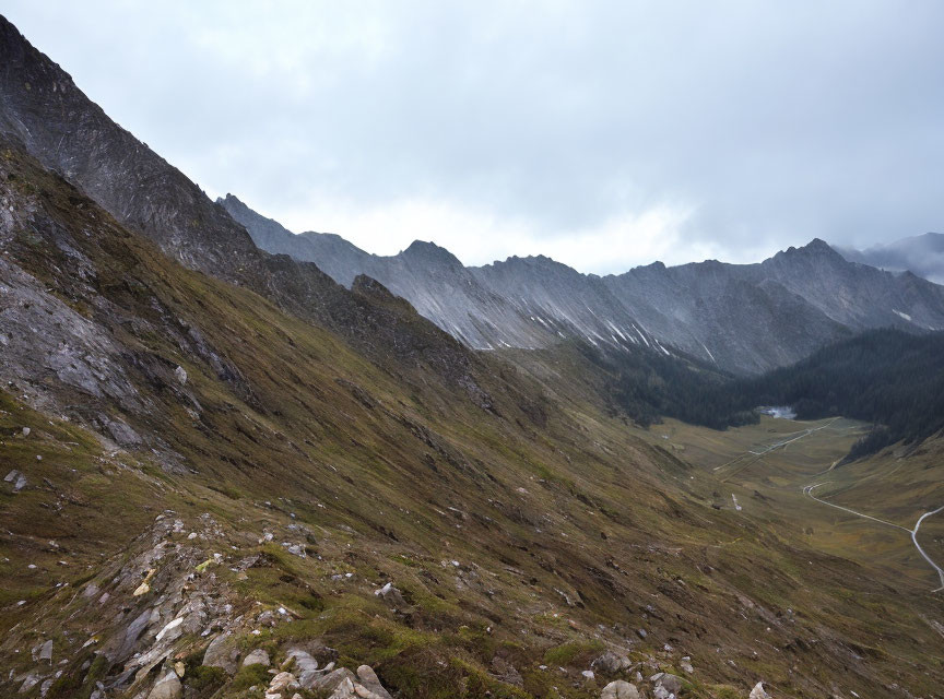 Overcast rugged mountain landscape with steep slopes and winding road.