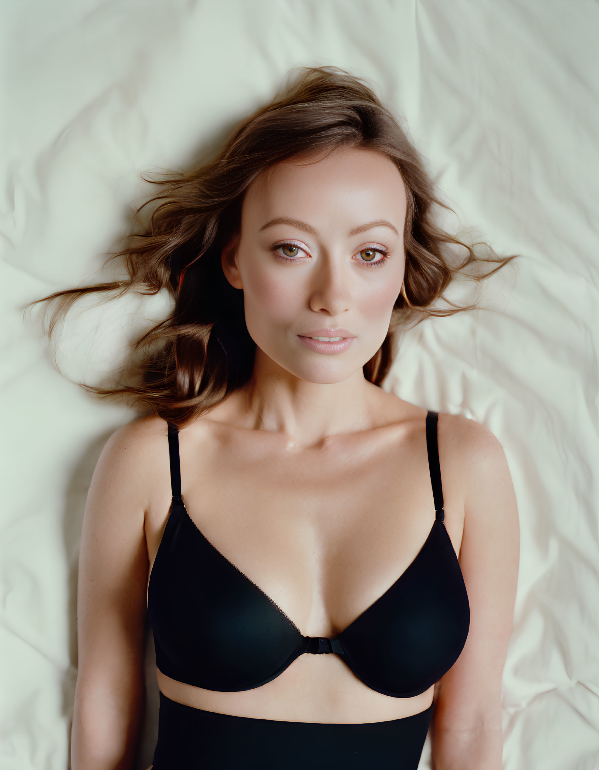 Dark-Haired Woman in Black Bra Lying on Cream-Colored Surface