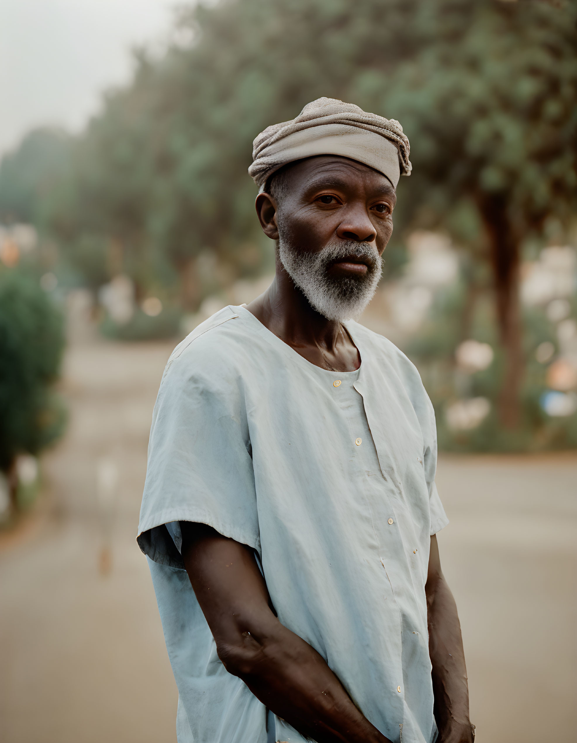 Elderly man with beard in light blue shirt and cap outdoors