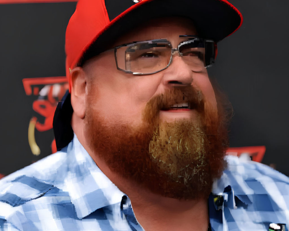 Bearded man in red cap and glasses smiling against logo backdrop