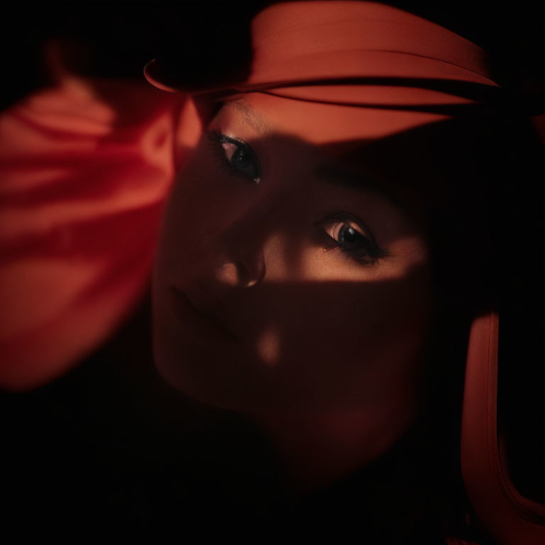 Face in shadows highlighted by warm red light, emphasizing piercing gaze