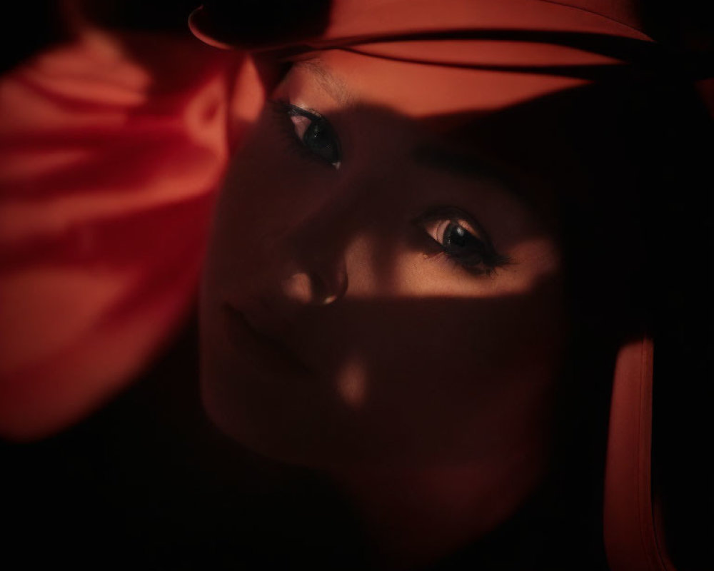 Face in shadows highlighted by warm red light, emphasizing piercing gaze