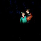 Person standing in dark forest with camera under beam of light and red flare effect