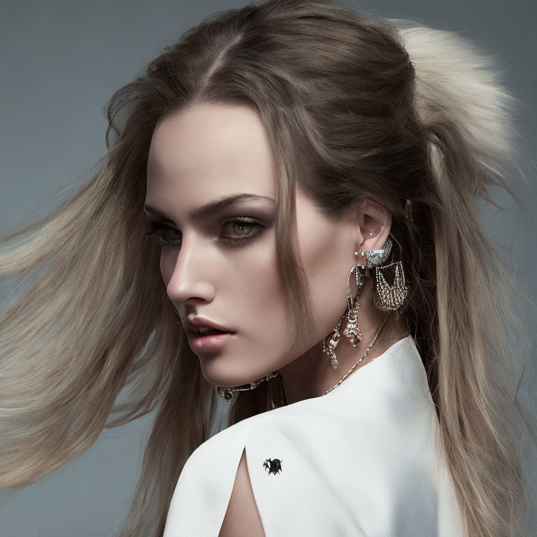 Woman with dramatic makeup, flowing hair, statement earrings, white garment, spider brooch