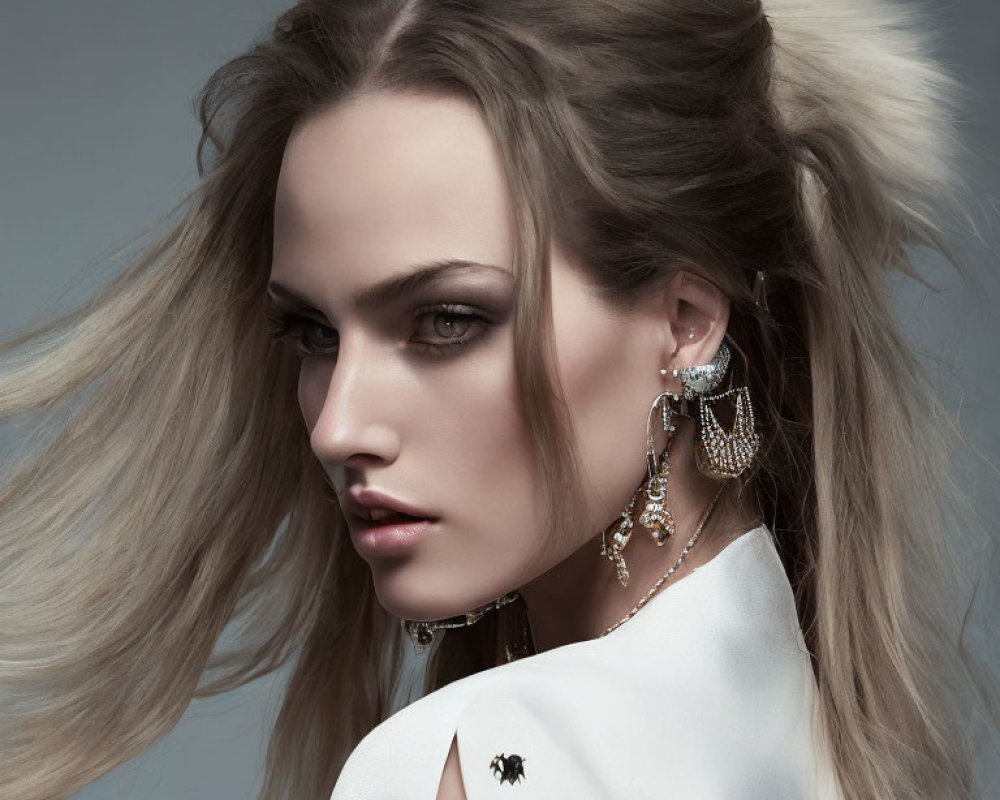 Woman with dramatic makeup, flowing hair, statement earrings, white garment, spider brooch