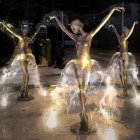 Three ethereal women dancing in glowing, flowery dresses in an enchanted garden at night.