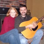 Happy couple in illustration playing guitar, woman leaning on man, smiling, with patterned background.