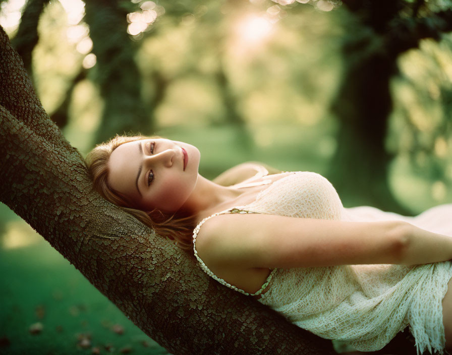 Woman in white dress lounging on tree branch in lush green setting