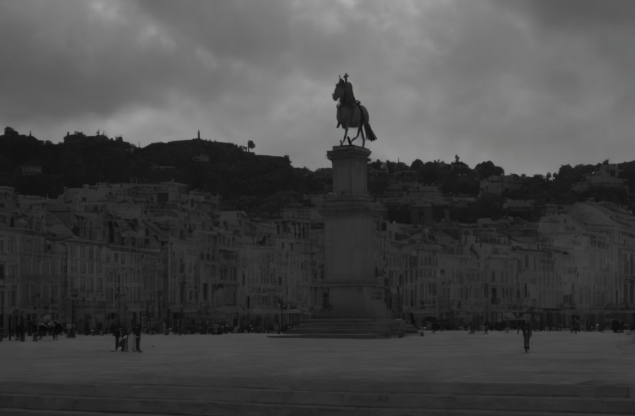 Monochrome statue on pedestal in open square with buildings and cloudy sky