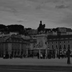 Monochrome statue on pedestal in open square with buildings and cloudy sky