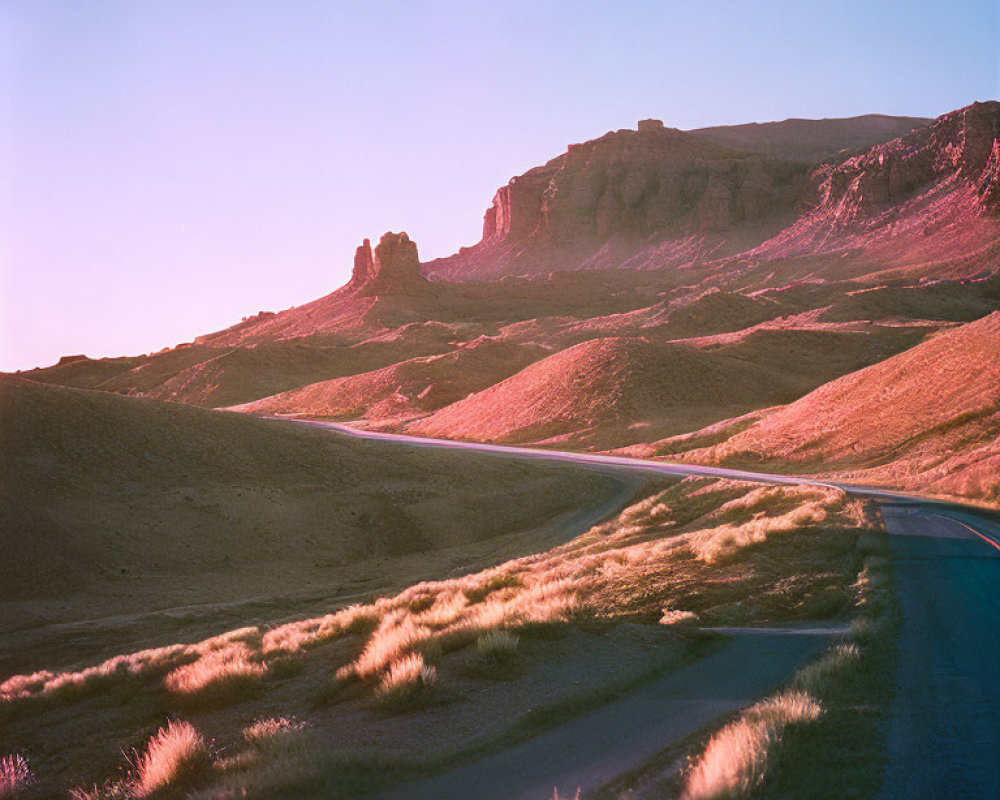 Serene desert landscape: winding road, sunset glow on rocks & grass