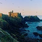 Vivid watercolor painting: Two castles on rocky cliffs above turbulent sea