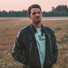 Man in teal shirt and black leather jacket in desert at dusk