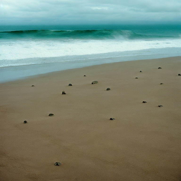 Tranquil beach scene with smooth waves, rocks, and cloudy sky