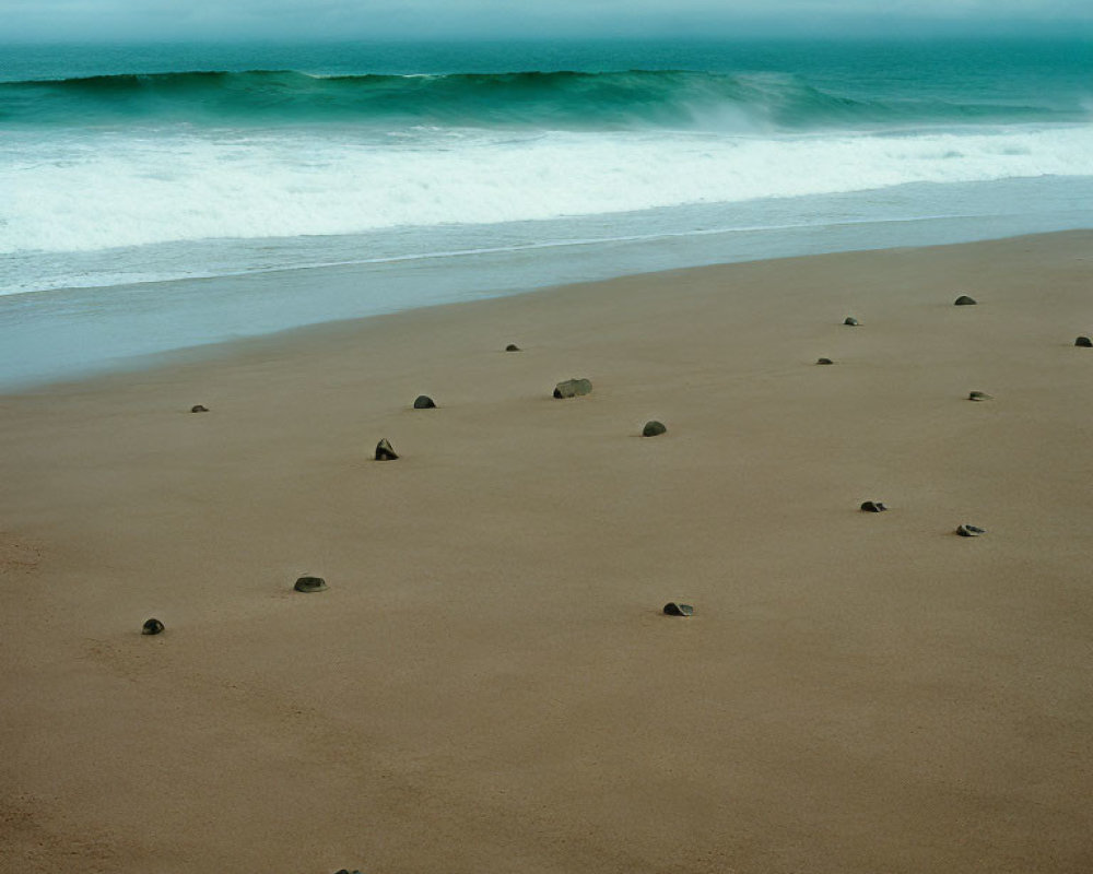 Tranquil beach scene with smooth waves, rocks, and cloudy sky