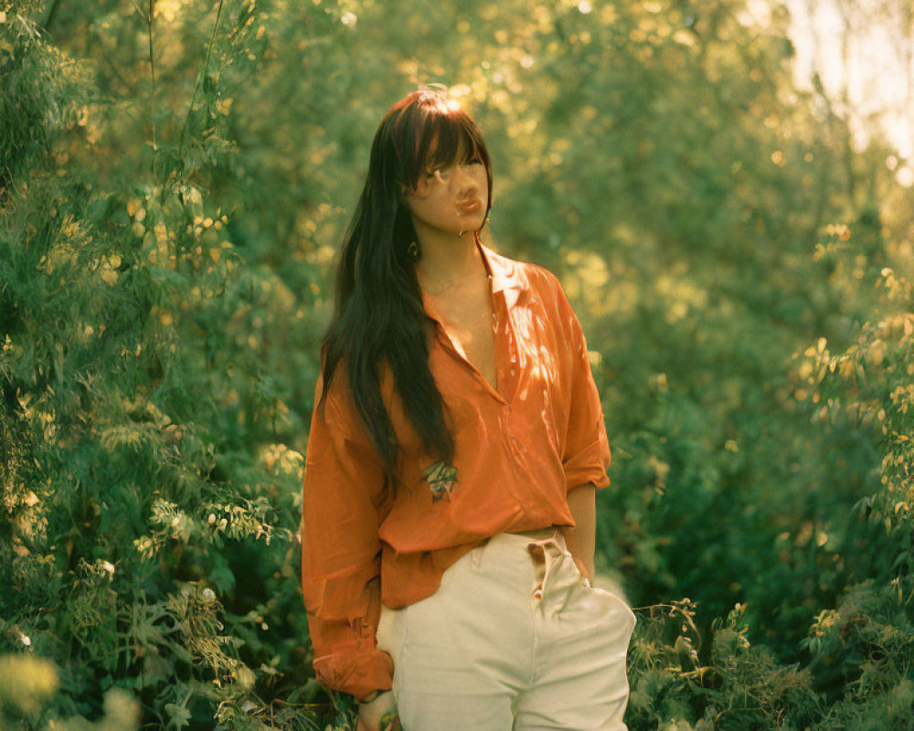 Woman in Orange Blouse and White Pants Surrounded by Greenery