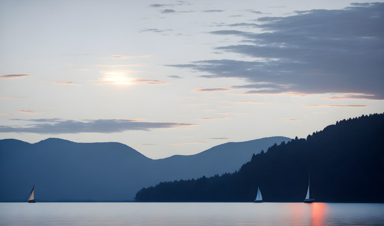 Sailboats on calm waters at dusk with silhouetted mountains