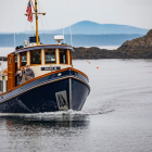 Vintage boat with blue hull near rocky shore and misty hills.