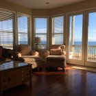 Sunlit living room with sea view, elegant furniture, wood floors, large windows, glass-paneled