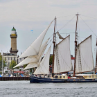 Sailboat with multiple masts and unfurled sails near coastline with lighthouse