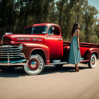 Vintage-dressed woman with headscarf by red pickup truck on tree-lined road