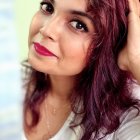 Purple-haired woman in white outfit with striking eyes and golden button collar