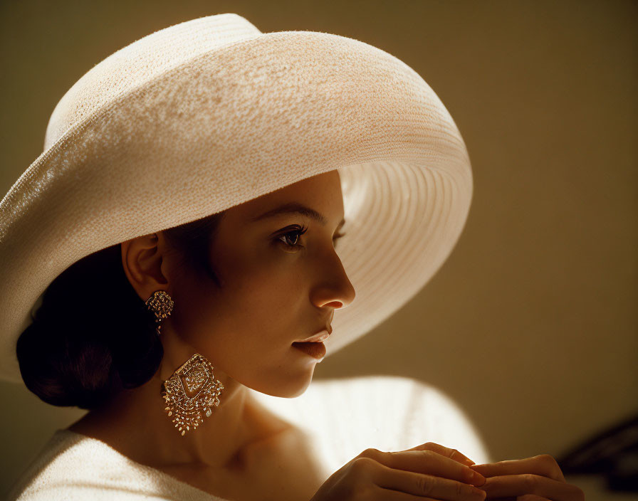 Profile of woman in wide-brimmed hat with ornate earrings in soft lighting