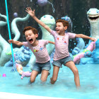 Children playing in shallow pool with colorful creatures and vibrant vegetation.