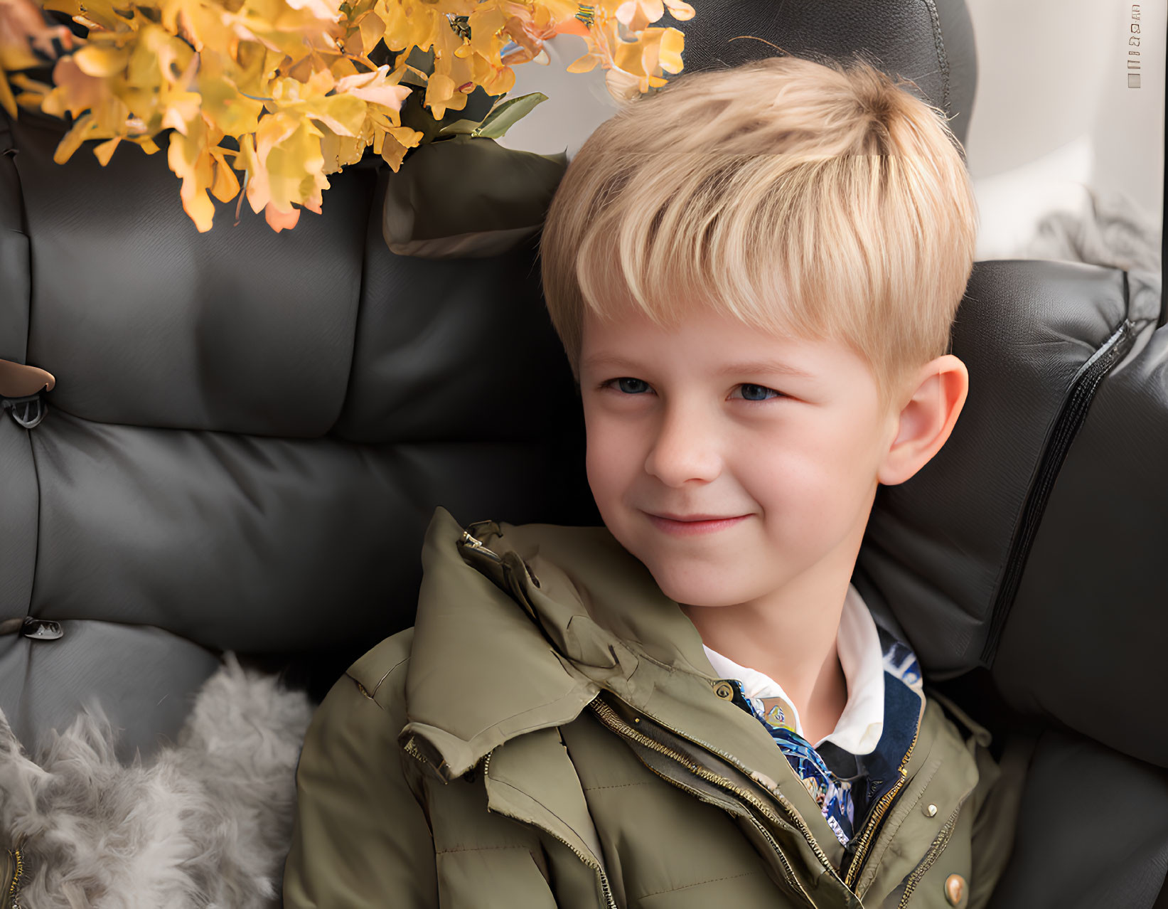 Blonde Boy in Green Jacket Smiling on Black Couch