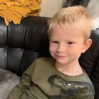 Blonde Boy in Green Jacket Smiling on Black Couch