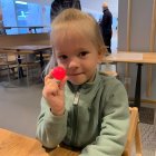 Child with ponytail holds red lollipop in bright room