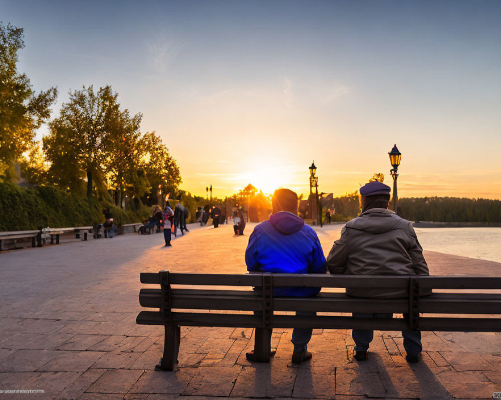 Two individuals on bench watching sunset with trees and path.