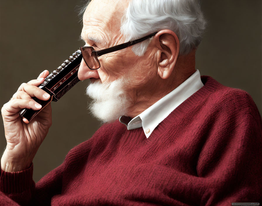 Elderly man with white beard playing harmonica in red sweater