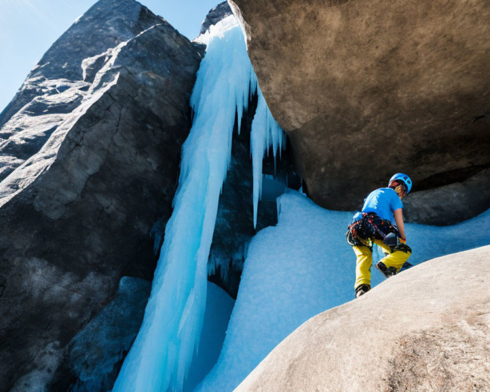 Climber in Blue Helmet Ascending Rocky Slope by Frozen Waterfall