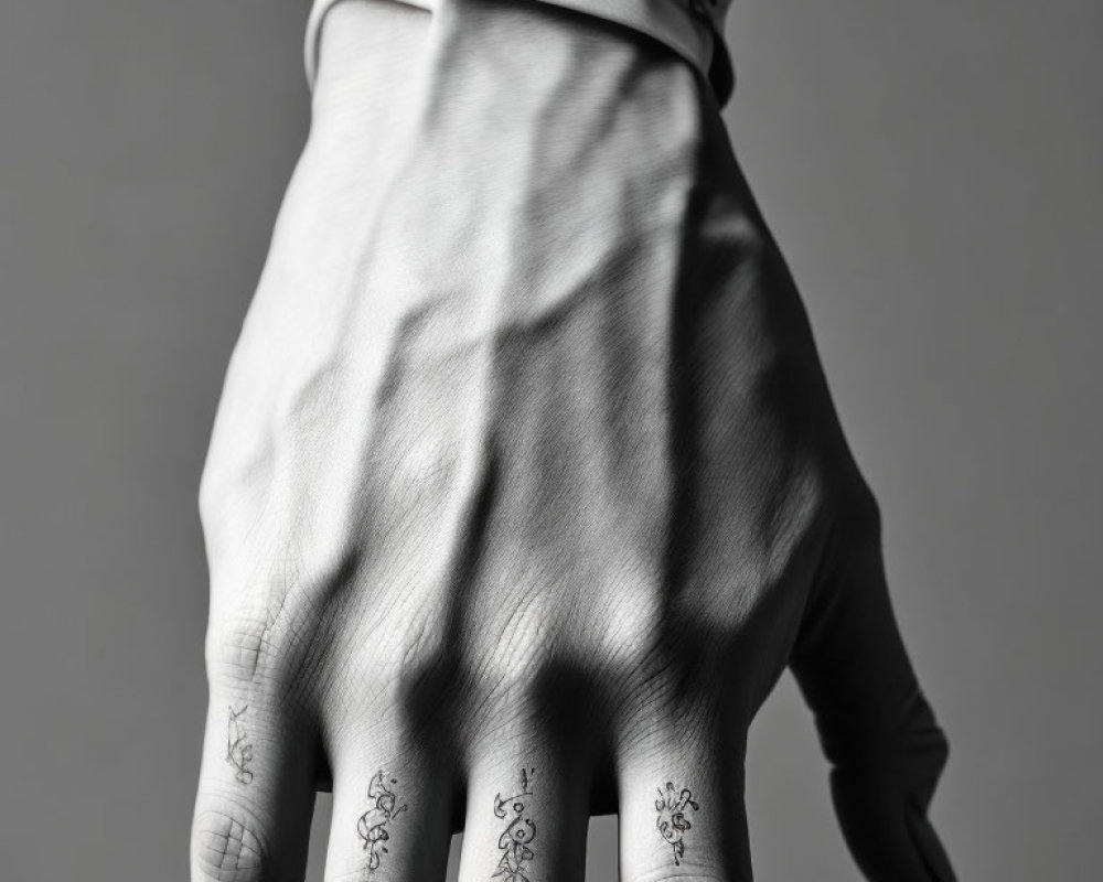 Monochrome photograph of hand with finger tattoos on solid background