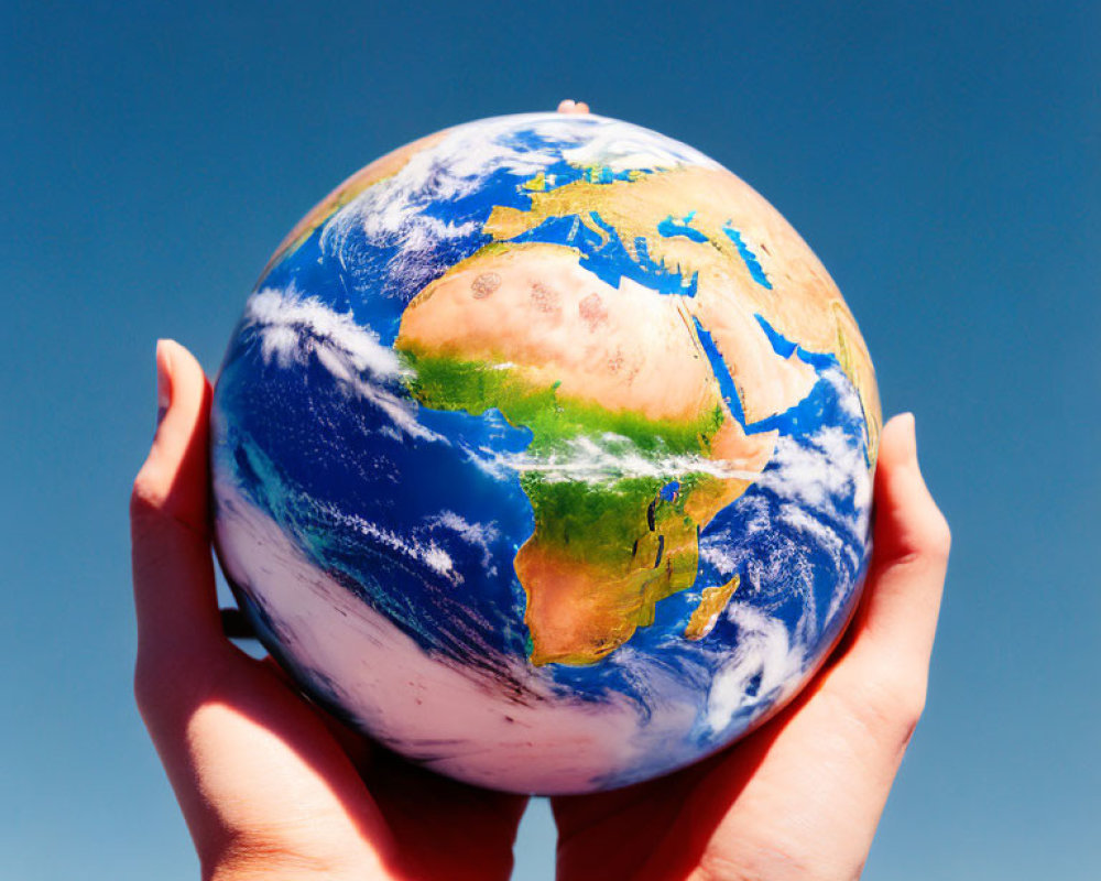 Hands Holding Globe Against Blue Sky