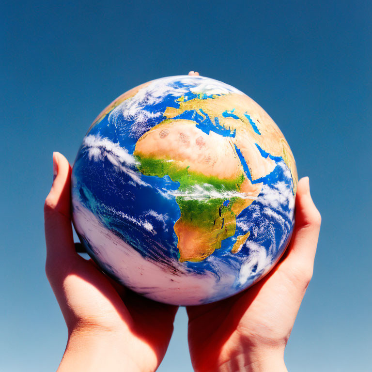 Hands Holding Globe Against Blue Sky