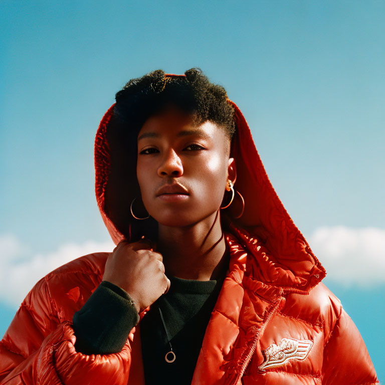 Young person in red puffer jacket under blue sky confidently gazes at camera