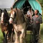 Ornate horses pulling covered wagon with passengers in lush landscape